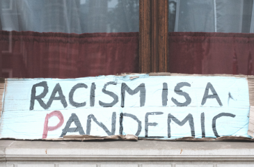 A painted cardboard sign that reads: Racism is a pandemic