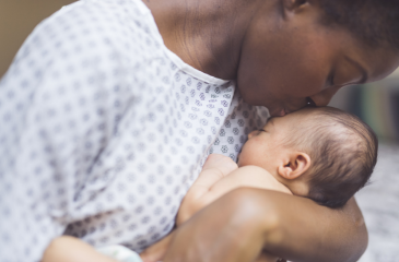 A black mother in a hospital gown kisses their new infant